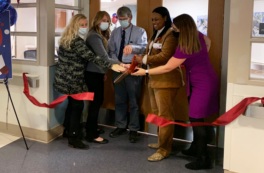 Five employees stand in the entryway of the Perinatal Evaluation and Treatment Unit, holding a large pair of scissors and cutting a red ribbon across the entrance